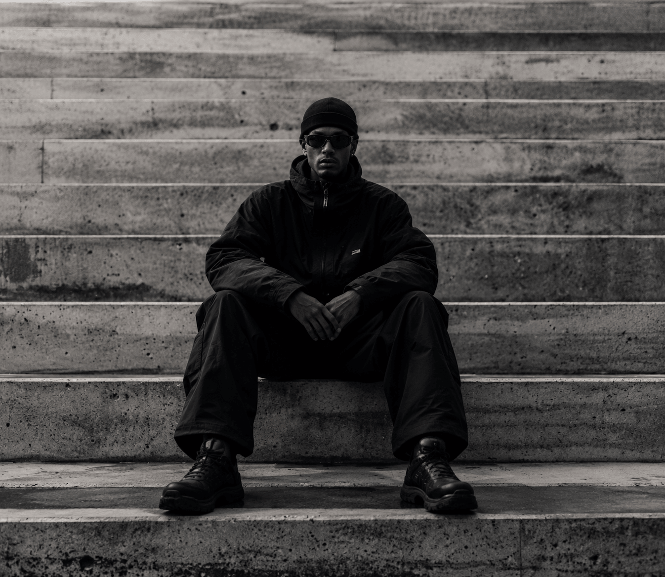 A model in a black shell and cargo trousers seated on concrete steps