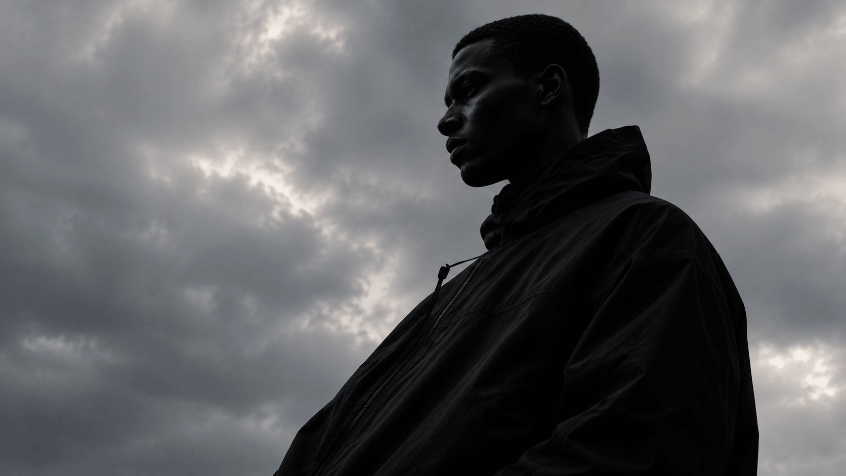 A model in a black shell jacket silhouetted against a stormy sky
