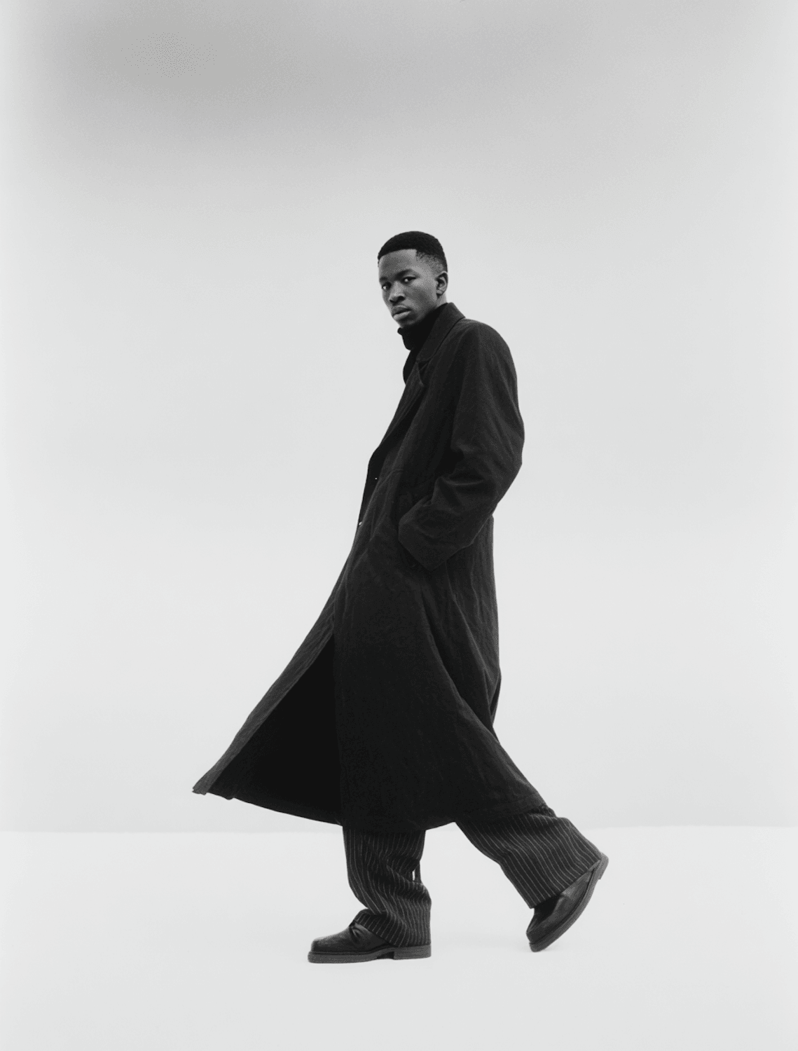 A man in a dark coat and pinstriped trousers mid-stride