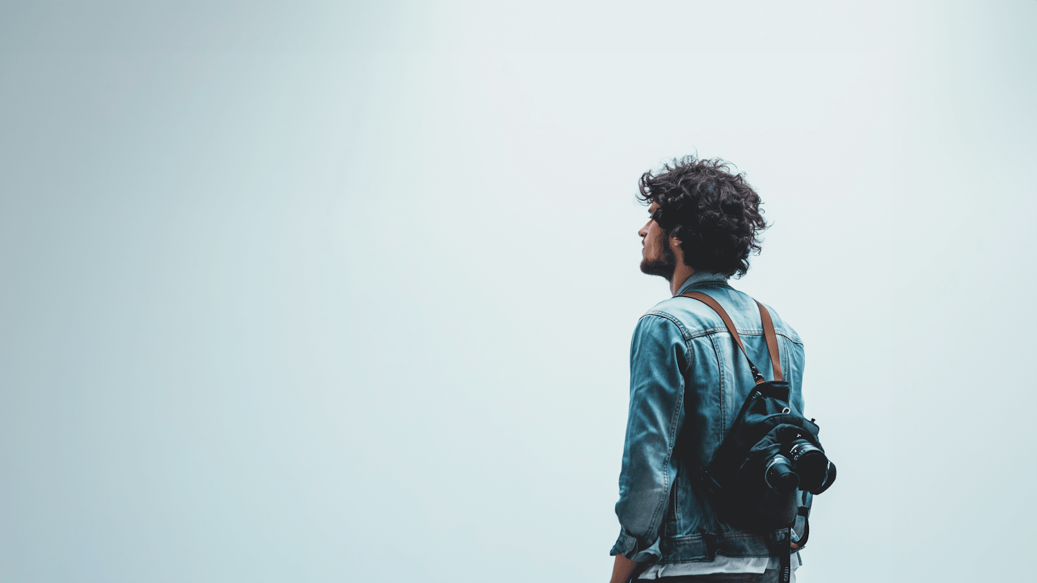 A man in a denim jacket carrying a camera, looking up